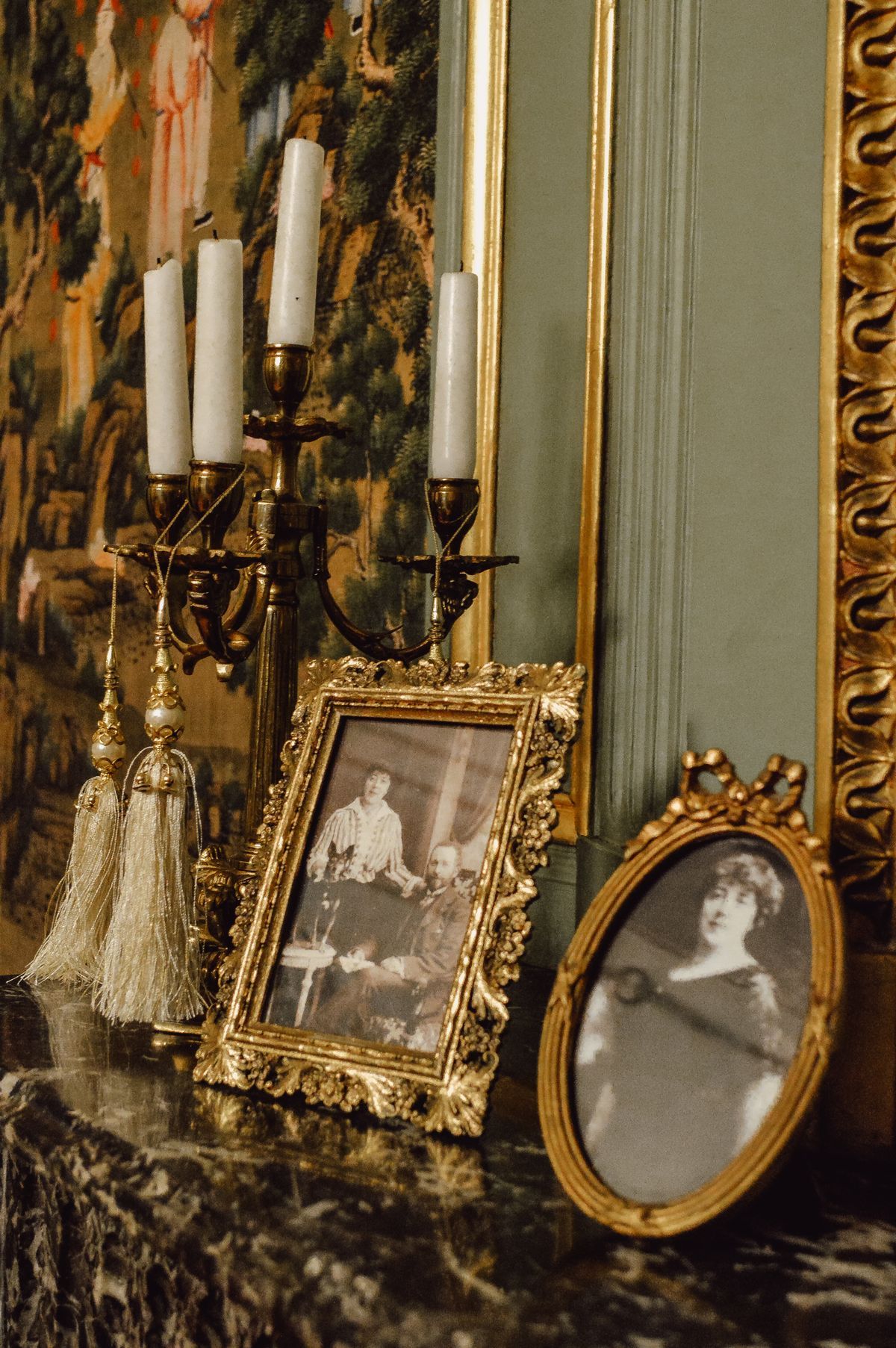 Cadres ornés et chandelier posés devant une tapisserie.